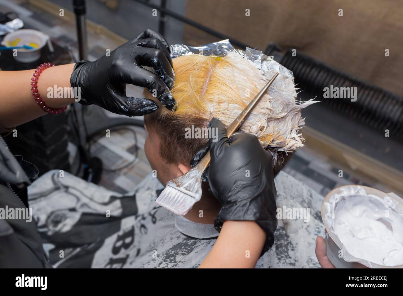 Die Hände einer professionellen Frau in Handschuhen halten beim Färben von Männerhaaren bei der Arbeit eine Bürste. Stockfoto