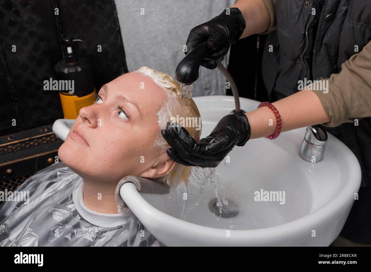 Eine Erwachsene, hübsche weiße Frau, die ihr Haar mit Regen wäscht, bevor sie in einem Friseursalon frisiert. Stockfoto