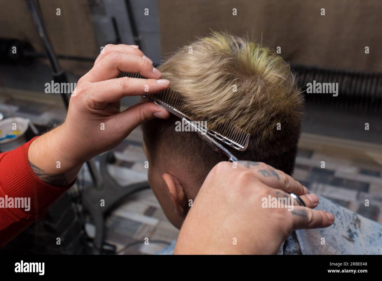 Die Hände eines professionellen männlichen Friseurs mit Schere und Kamm schneiden einem Salonkunden bei der Arbeit die Haare ab. Stockfoto