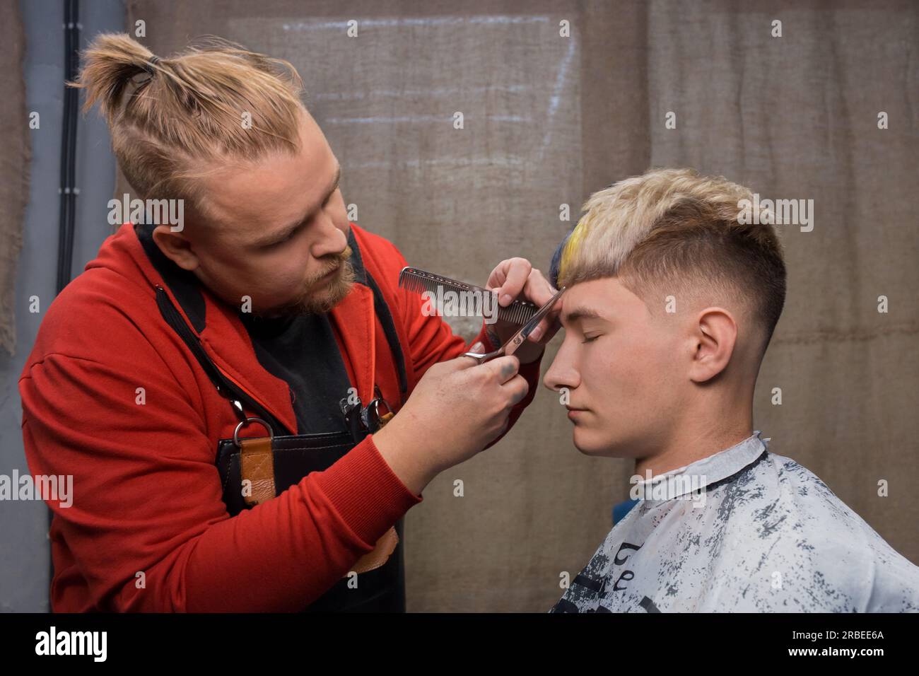Modischer erwachsener Mann, Kaukasier, Friseur, der für einen jungen Mann Pony mit Schere schneidet, ein Kunde mit einer coolen, stilvollen Frisur, bob, Farbkreati Stockfoto