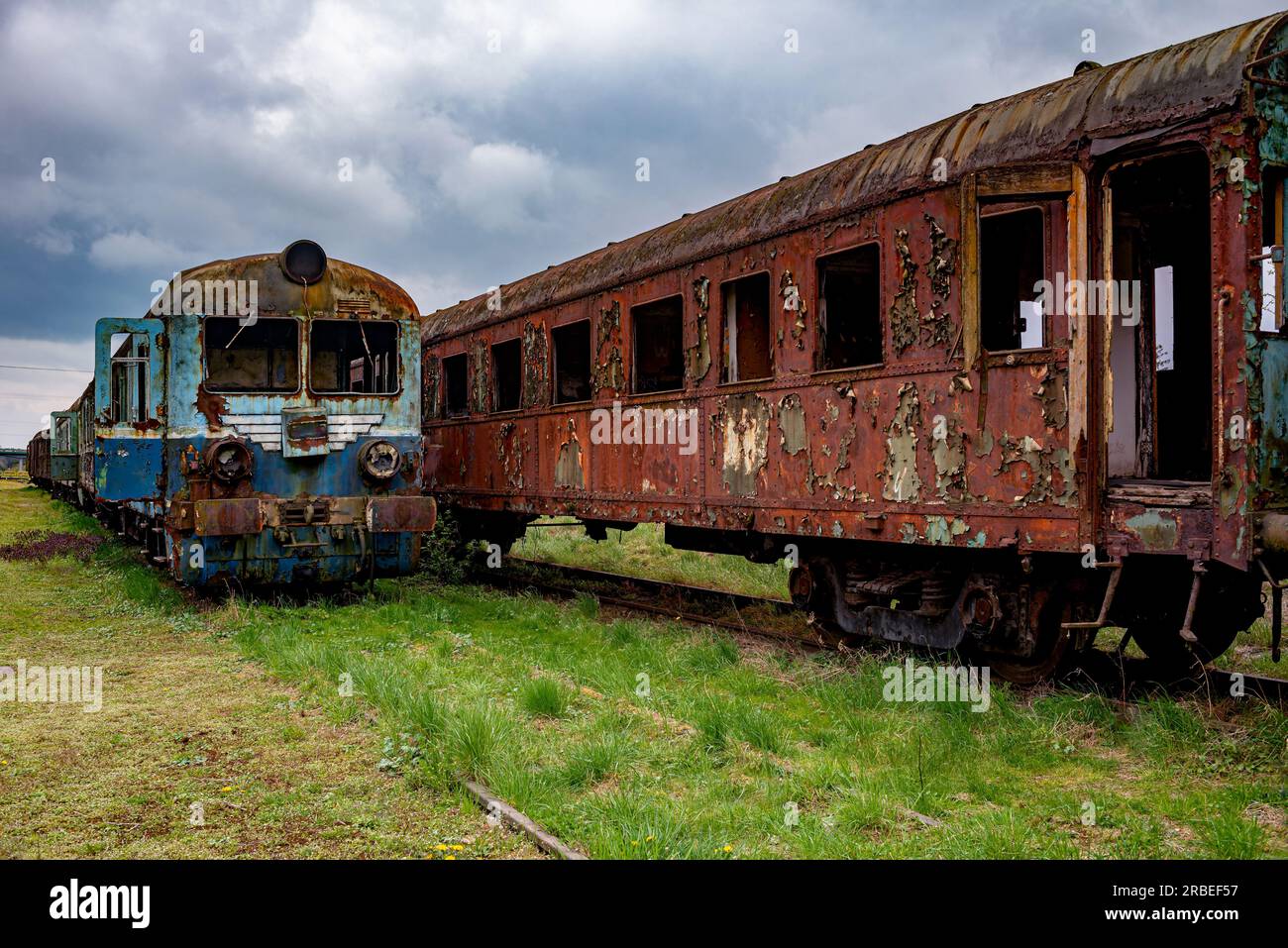 Alte, beschädigte EWU und rostige Pkw, die auf dem Bahngleis auf grünem Grasfeld stehen gelassen wurden Stockfoto