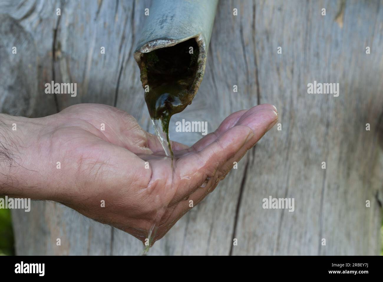 Wenn das Wasser aus dem Brunnen ausläuft. Eine menschliche Hand fängt das einzige spärlich fließende Wasser am Brunnen. Stockfoto