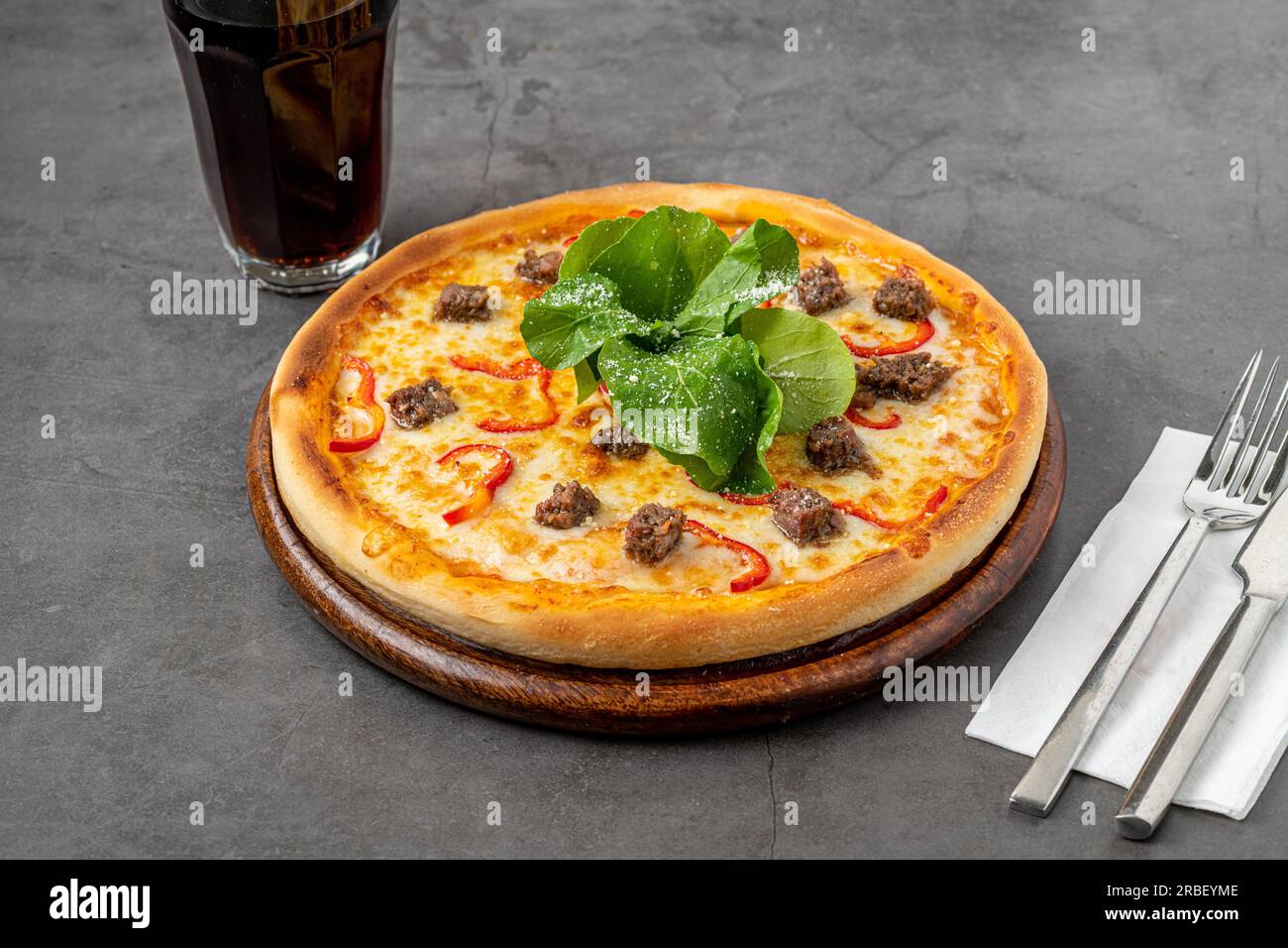 Pizza mit Paprika und Roastbeef auf dem Schneidebrett auf einem Steintisch Stockfoto