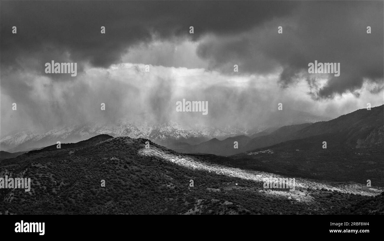 Ein Moment, in dem an einem stürmischen Tag in der Provinz von Südkreta eine Lichtlinie auftauchte. Im Hintergrund liegen die schneebedeckten Berge von Psiloritis. Stockfoto