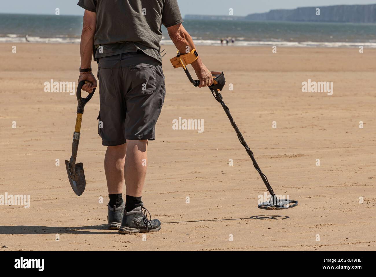 Ein Mann mit einem Metalldetektor und einem kleinen Spaten am Strand Stockfoto
