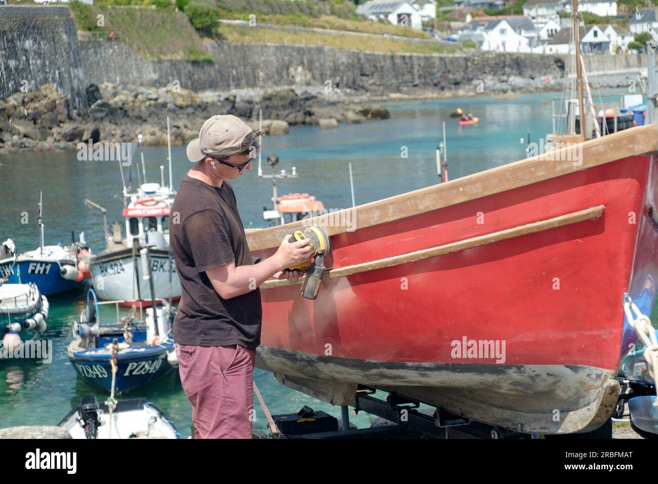 Coverack ist ein Fischerdorf am Meer auf der Eidechsenhalbinsel in Cornwall, Großbritannien. Ein junger Mann, der ein Boot am hafen von coverack wartet Stockfoto