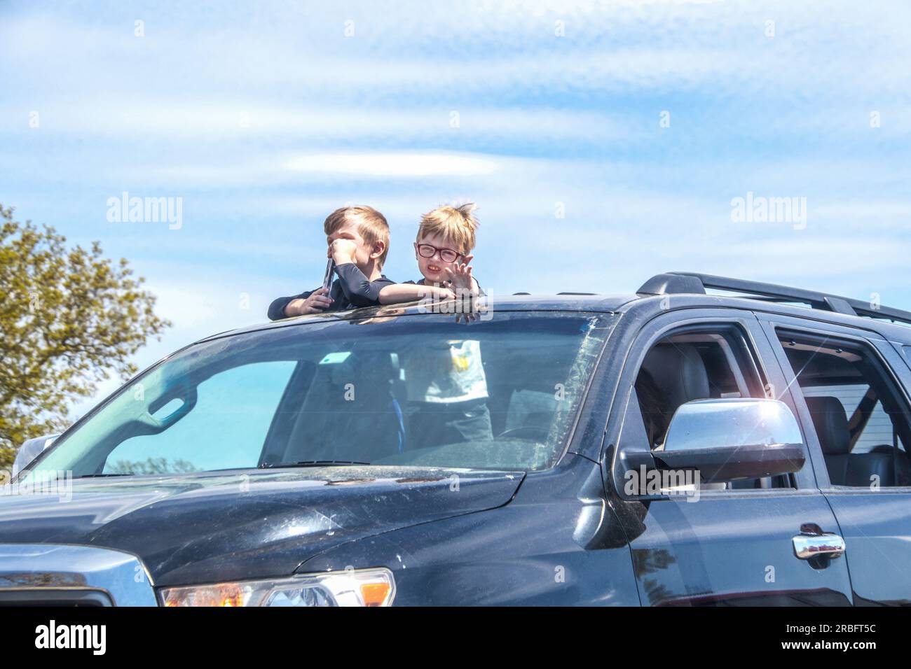 04-15-2020 Bartlesville USA - zwei junge Brüder im SUV mit aus dem Schiebedach ragenden Köpfen, die durch die Natur fahren - einer mit Brillenwellen - Stockfoto