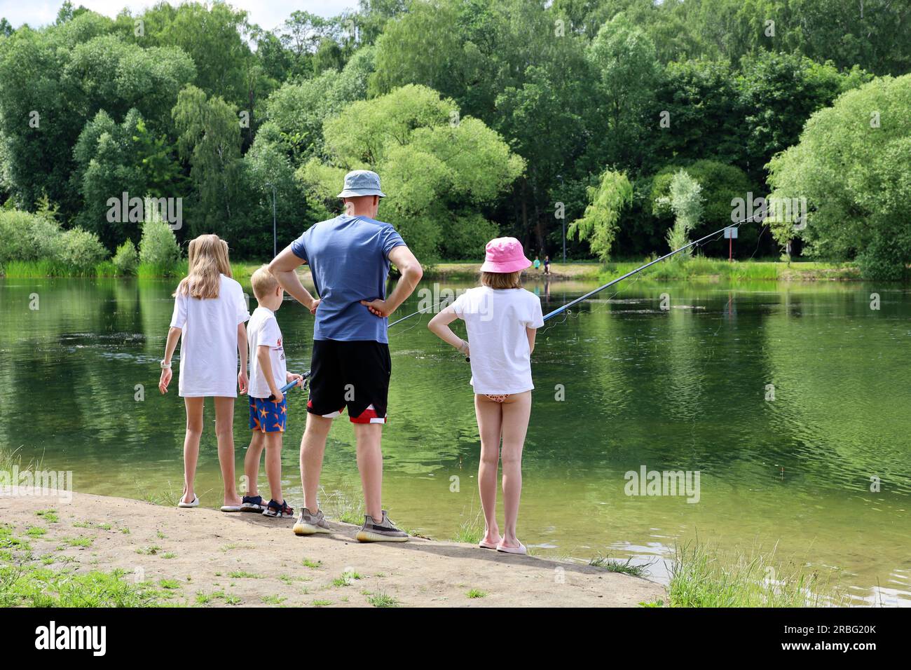 Mann und Kinder angeln an einem Seestrand. Vater mit kleinen Söhnen und Töchter mit Angelrute, Sommerurlaub am Wasser Stockfoto