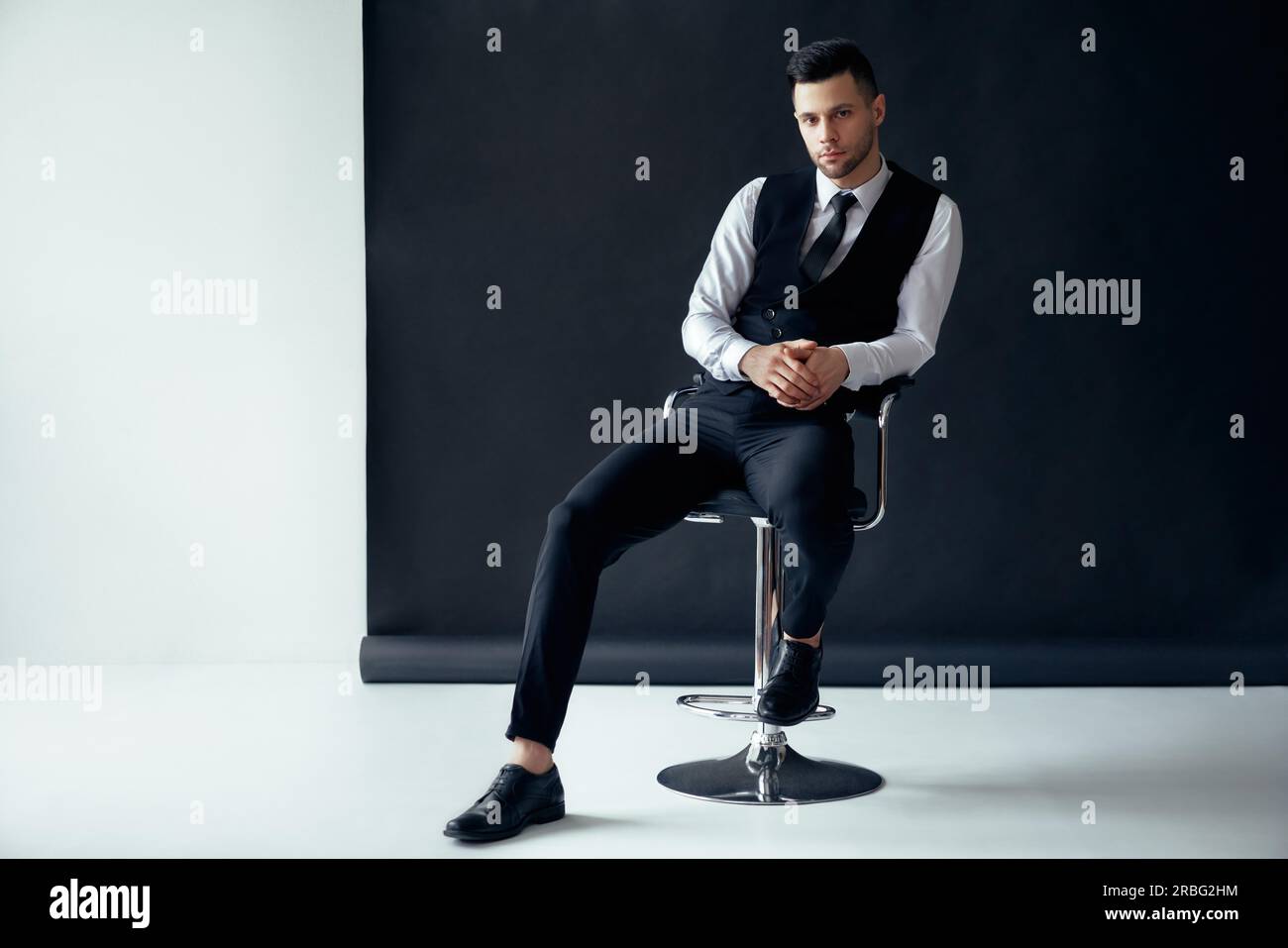 Elegante zuversichtlich Mann posiert und sitzen auf den Stuhl, der auf schwarzen und weißen Hintergrund. erfolg konzept Stockfoto
