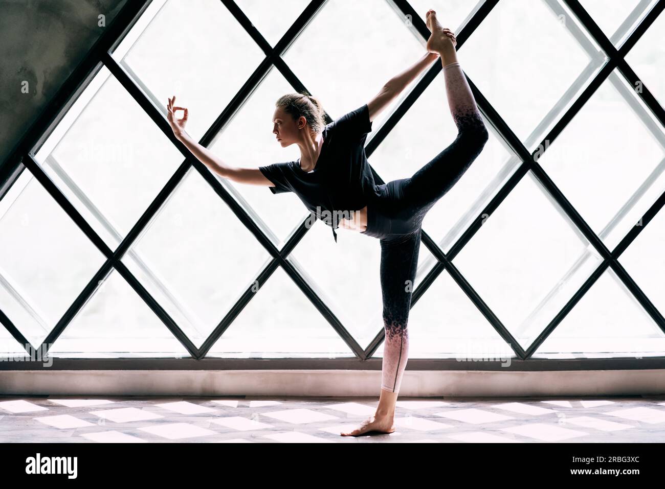 Junge wunderschöne Frau, die Yoga asana natarajasana auf einem großen dreieckigen Fensterhintergrund macht. Wohlbefinden, Meditation und gesunder Lebensstil. Herr des Tanzes Stockfoto