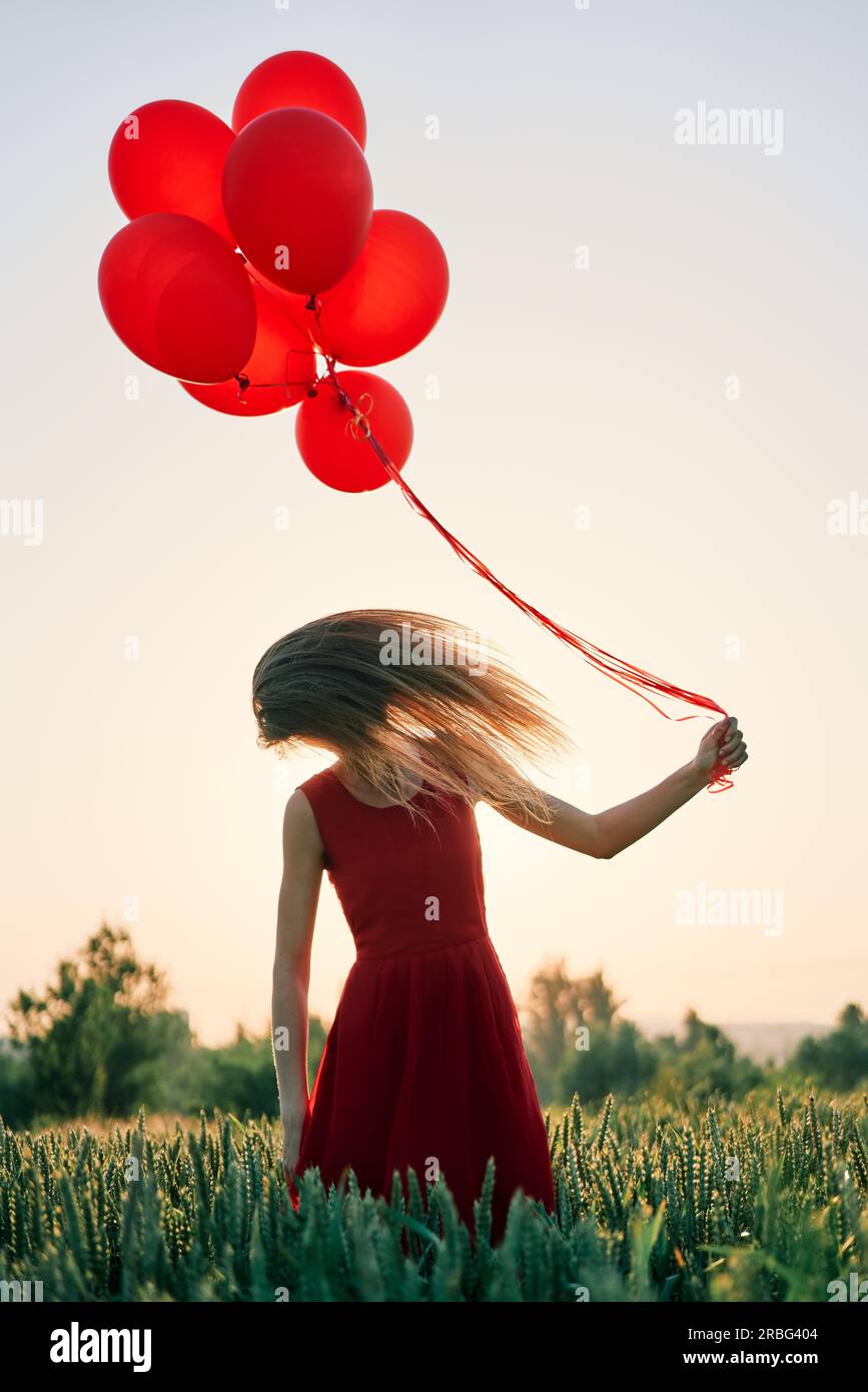Junge Frau schüttelte ihren Kopf mit ihrem Haar Fliegen um Sie herum und halten roten Ballons Stockfoto