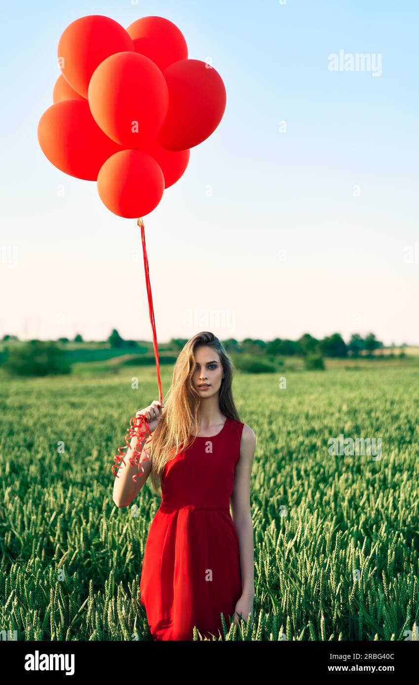 Junge schöne Frau im roten Kleid in grün mit roten Ballons posieren. Freiheit, Spaß, Ferienhäuser Konzept Stockfoto