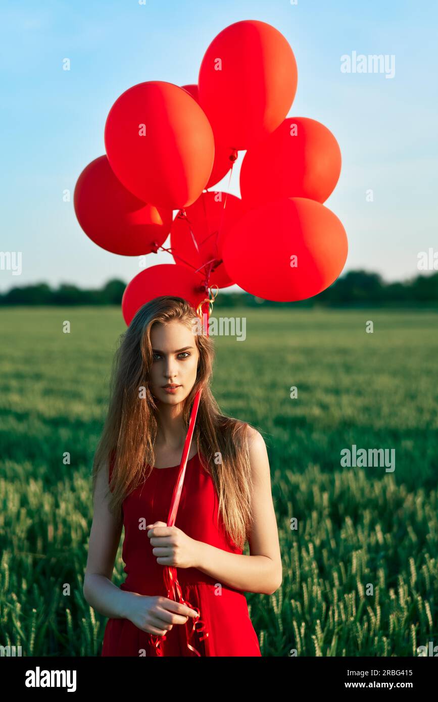 Junge schöne Frau im roten Kleid in grün mit roten Ballons posieren. Freiheit, Spaß, Ferienhäuser Konzept Stockfoto