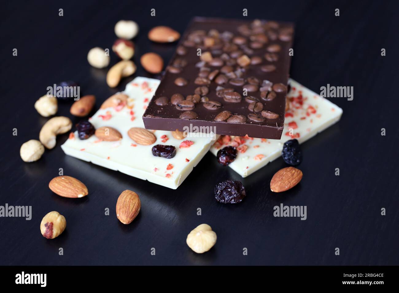 Weiße und dunkle Schokolade mit getrockneten Rosinen, Kaffeebohnen und Nüssen. Leckeres Dessert auf einem dunklen Holztisch Stockfoto
