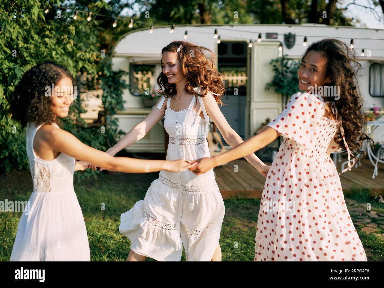 Gerne schöne Frauen tanzen im Kreis während ein Picknick. Multi-ethnische Mädchen Spaß zusammen haben im Freien. Kaukasier, afrikanische amerikanische und asiatische Mädchen Stockfoto