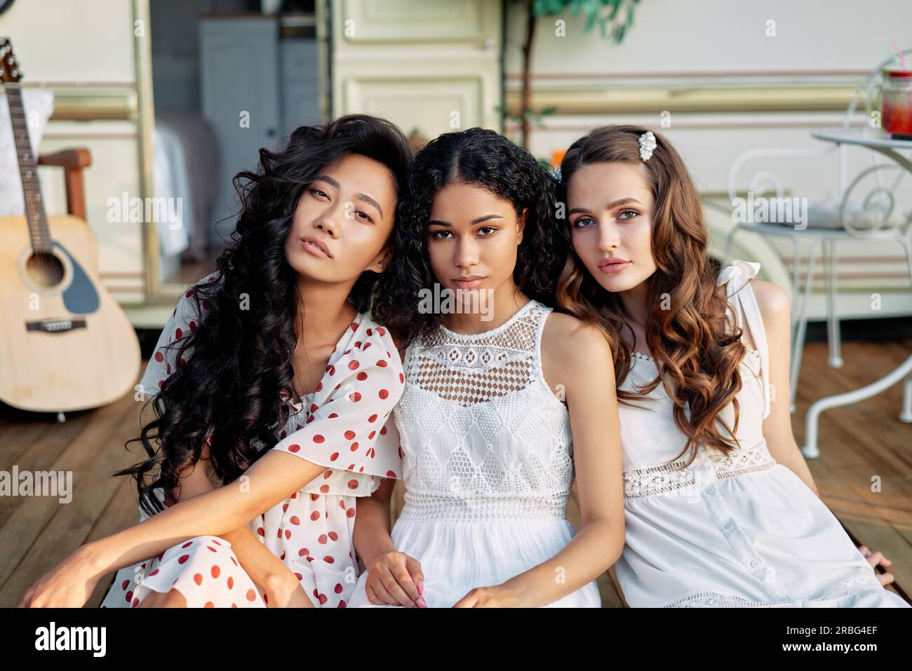 Wunderschöne, multiethnische Mädchen, die sich in der Nähe eines Wohnwagens im Freien posieren. Kaukasische, afroamerikanische und asiatische Mädchen haben Spaß bei einem Picknick. Frauen Stockfoto