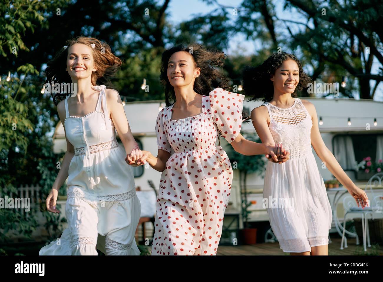 Fröhliche, wunderschöne Frauen, die beim Picknick im Freien laufen und Spaß haben. Multiethnische Mädchen, weiße, afroamerikanische und asiatische Mädchen Stockfoto