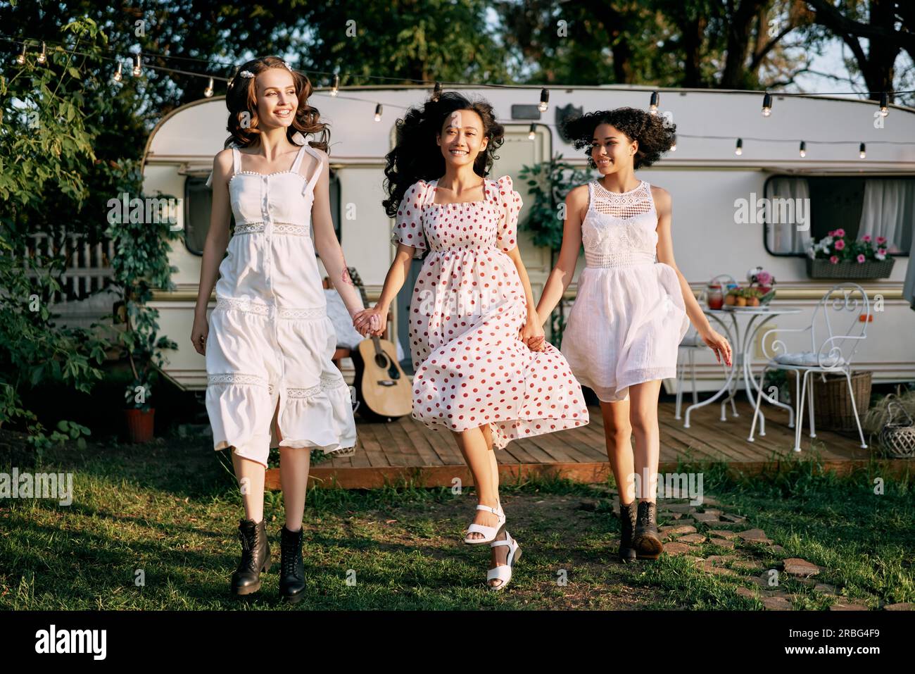 Fröhliche, wunderschöne Frauen, die beim Picknick im Freien laufen und Spaß haben. Multiethnische Mädchen, weiße, afroamerikanische und asiatische Mädchen Stockfoto