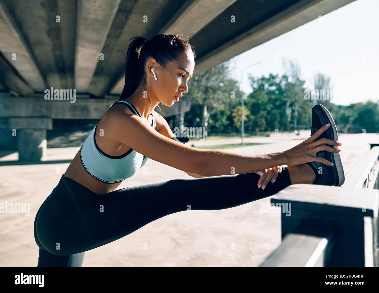 Sportlicher Damenläufer, der die Beine streckt, um sich vor dem Training aufzuwärmen. Urbanes Trainings- und Laufkonzept Stockfoto