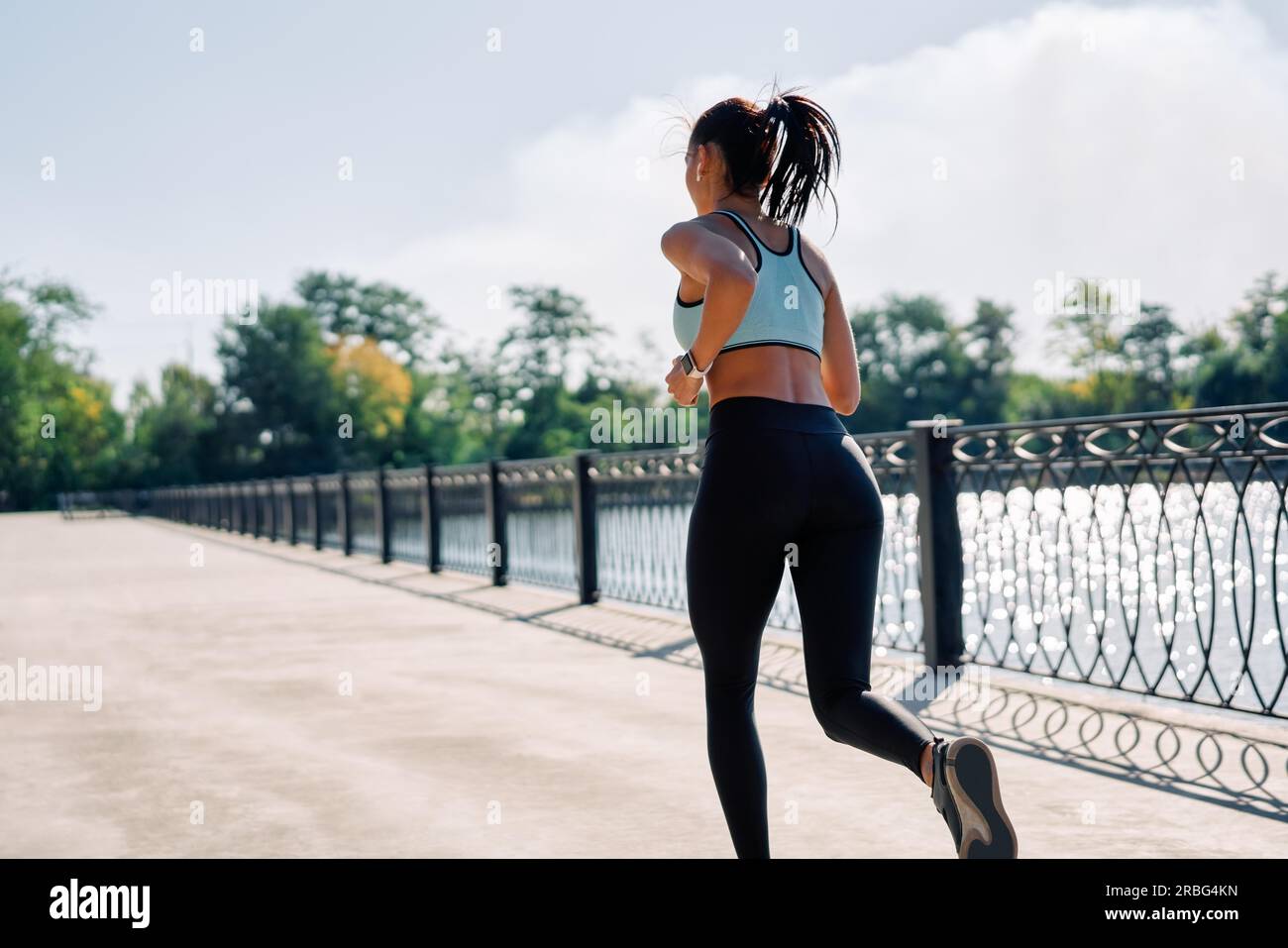 Rückansicht einer fitten Frau, die draußen am Fluss rennt. Schöne Frau in Sportbekleidung, die draußen joggt. Dynamische Bewegung Stockfoto
