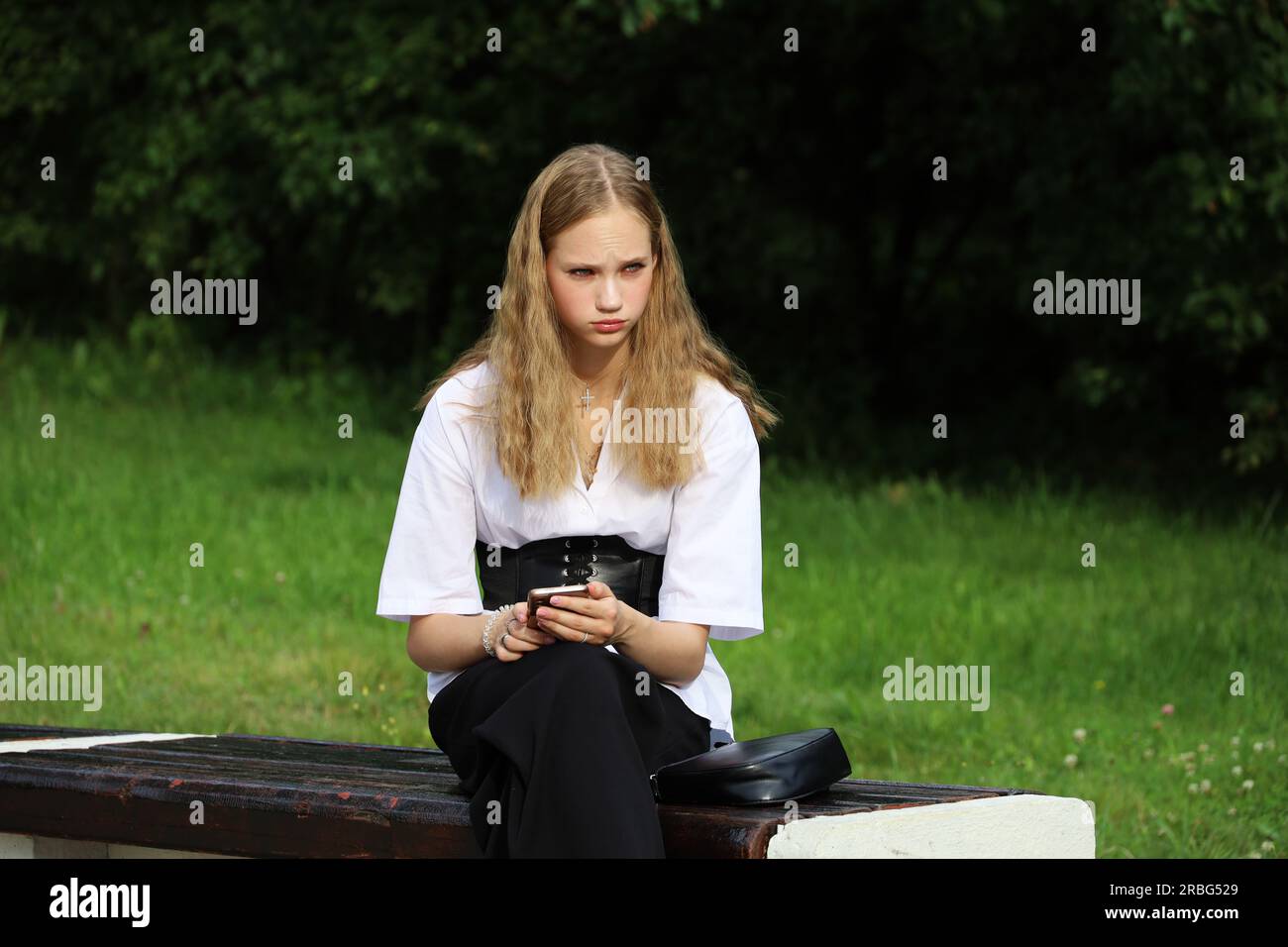 Blondes Mädchen, das auf einer Bank sitzt, mit Smartphone in der Hand Stockfoto