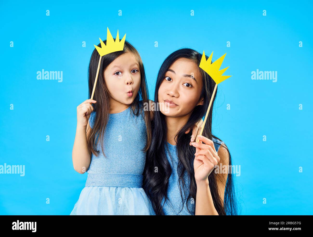 Mutter und süße kleine Tochter mit einer Papierkrone auf Stick auf blauem Hintergrund haben Spaß zusammen. Happy lustige Familie Konzept Stockfoto