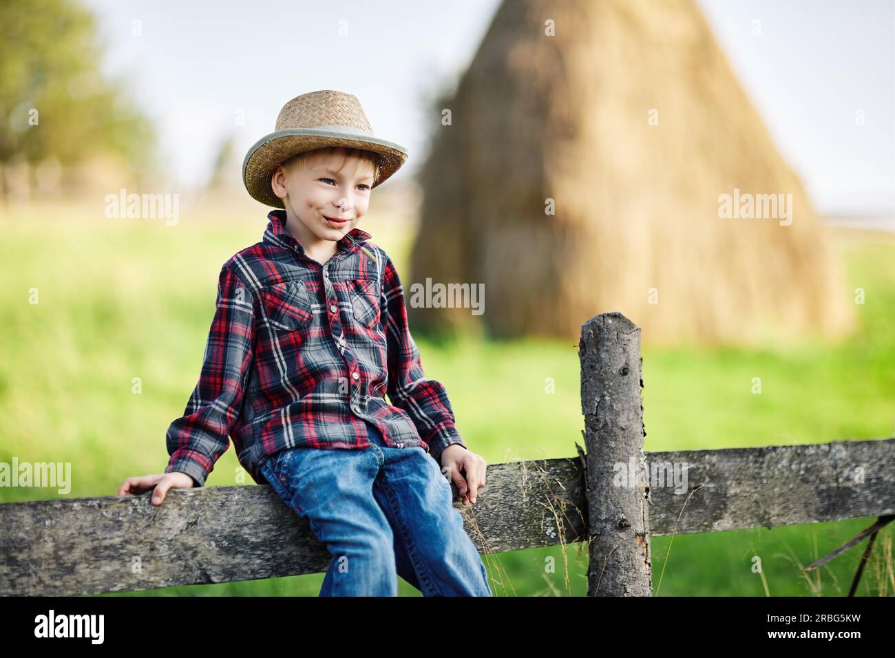 Nahaufnahme eines kleinen Jungen in einer Hutsitzungauf einem Holzzaun Stockfoto