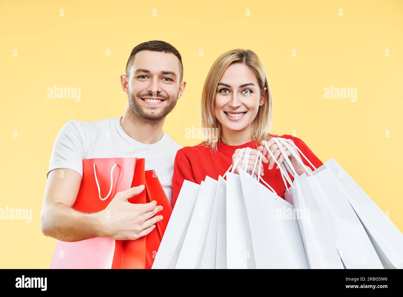 Junge glückliche Paar hält Einkaufstaschen in den Händen über gelben Hintergrund. Verkauf, äher, Kunde, Rabatt-Konzept Stockfoto