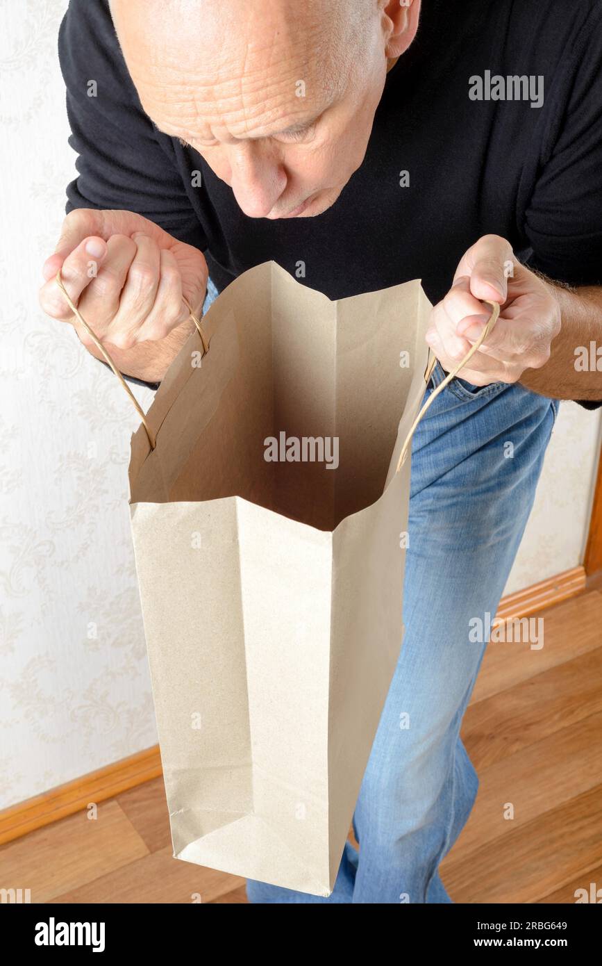 Ein Mann in Jeans und schwarzem Sweatshirt sucht in einer braunen Papiertüte Stockfoto