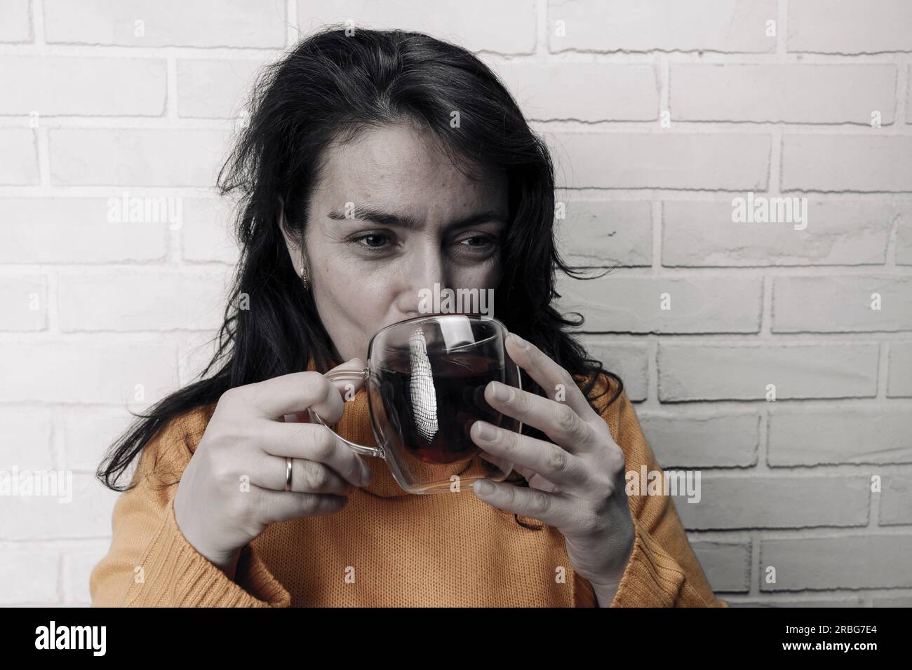 Eine hübsche weiße Frau mittleren Alters nach Stress stellt ihr mentales Gleichgewicht mit einer Tasse heilenden Tee wieder her. Glasdurchsichtiger Becher mit köstlichem Duft Stockfoto