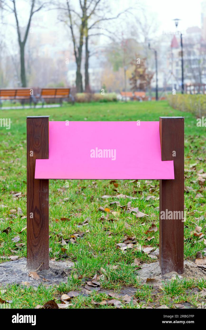 Leere rosa Holzbrett für Informationen und Angaben in den Park, mit einem Hintergrund von grünem Gras durch die Blätter im Herbst fallen Stockfoto