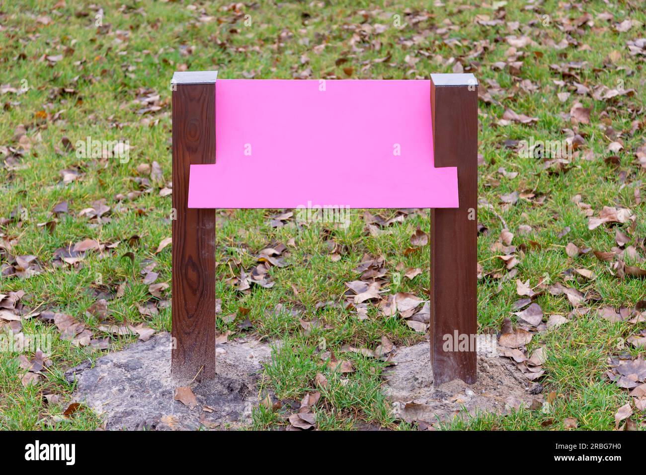 Leere rosa Holzbrett für Informationen und Angaben in den Park, mit einem Hintergrund von grünem Gras durch die Blätter im Herbst fallen Stockfoto