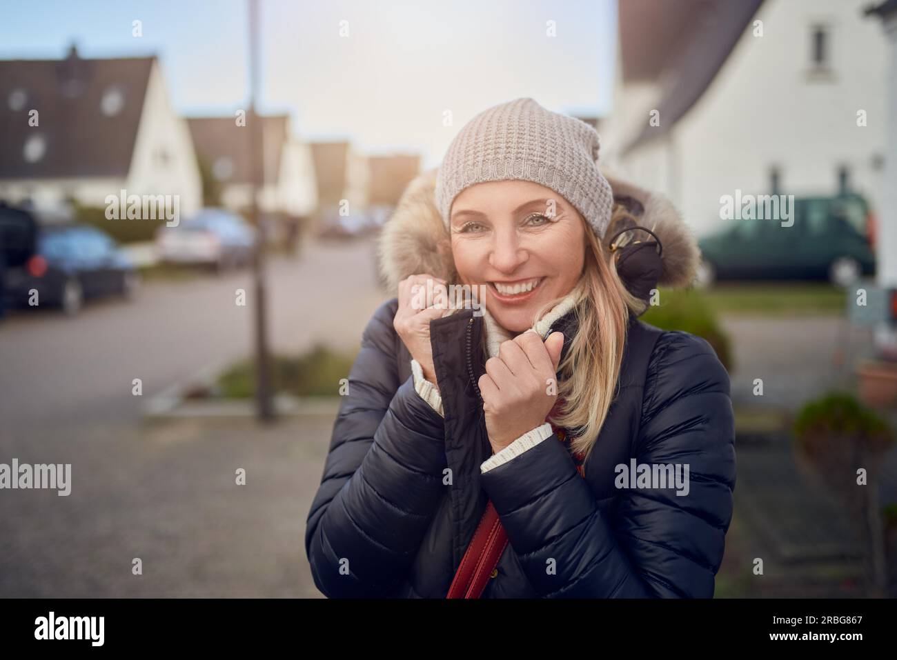 Lächelnd glücklich Frau mittleren Alters stehen im Freien an einem kalten Wintertag in eine warme Jacke und gestrickte Mütze in einer Vorstadtstraße Stockfoto