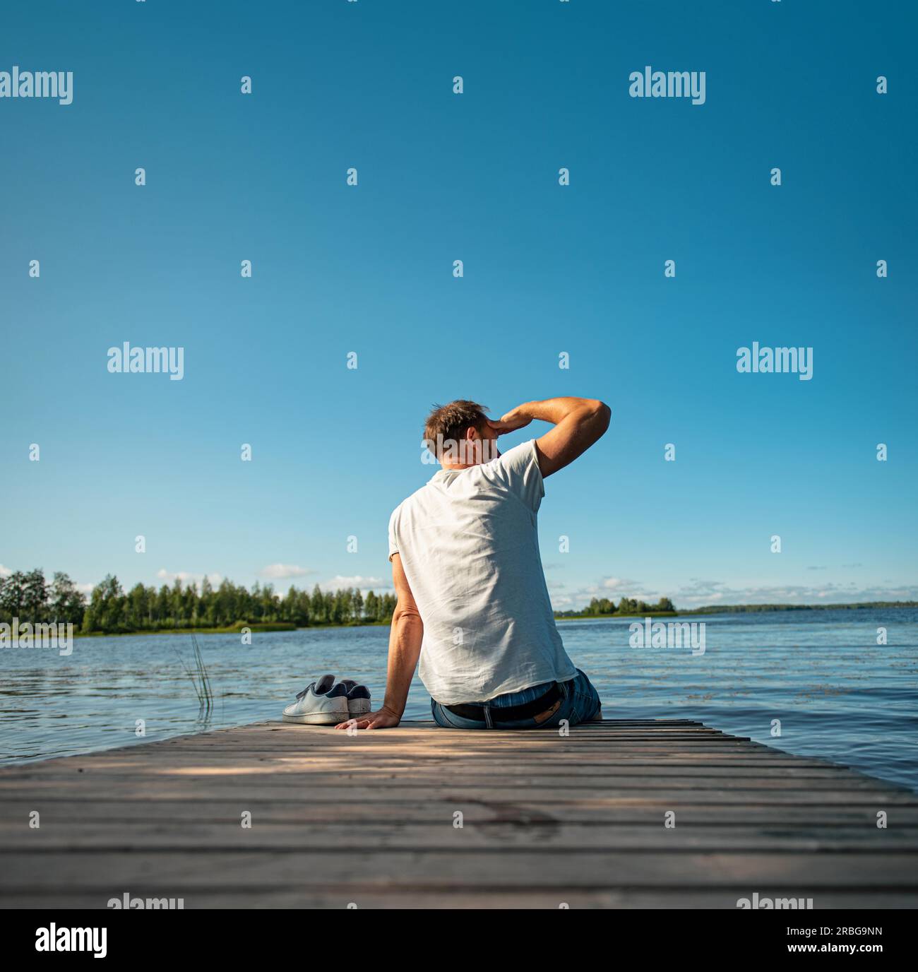 Ein Mann, der im Sommer in Finnland auf einem hölzernen Steg am See sitzt Stockfoto