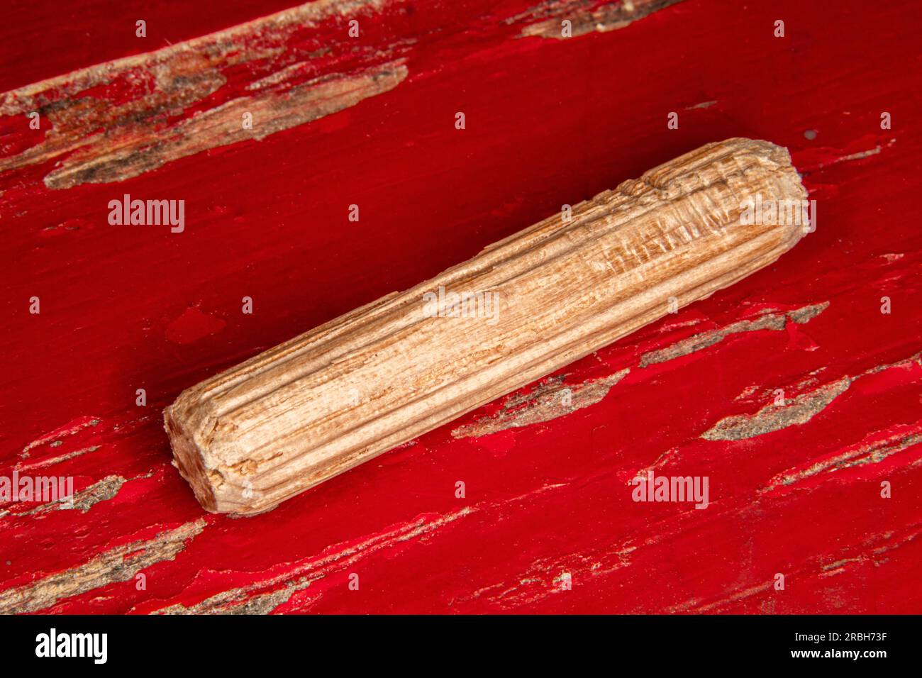 Einzelne Eichenholz-Passstifte auf rot lackiertem abgenutzten Hintergrund, Passstifte werden verwendet, um zwei Holzstücke zu verbinden, Verbindung, Schreiner Stockfoto