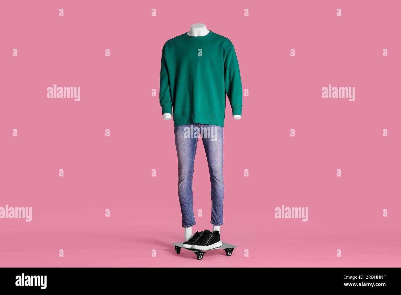 Männliche Schaufensterpuppe mit Turnschuhen in grünem Sweatshirt und Jeans auf pinkfarbenem Hintergrund. Stylisches Outfit Stockfoto