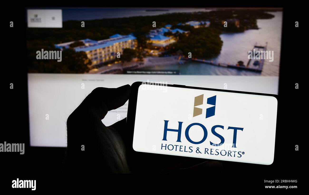 Person, die ein Mobiltelefon mit dem Logo des US-Unternehmens Host Hotels and Resorts Inc. Auf dem Bildschirm vor der Unternehmenswebseite hält. Konzentrieren Sie sich auf das Display des Telefons. Stockfoto