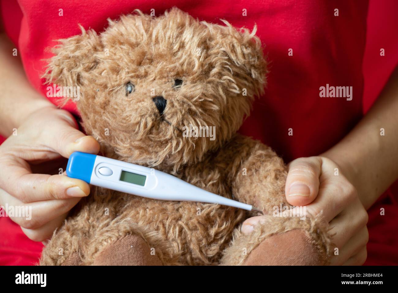 Mädchen hält einen braunen Teddybären mit einem Thermometer in der Hand zu Hause im Schlafzimmer auf dem Bett, Kindermorbidität, Fieber und Fieber, weltweit pand Stockfoto