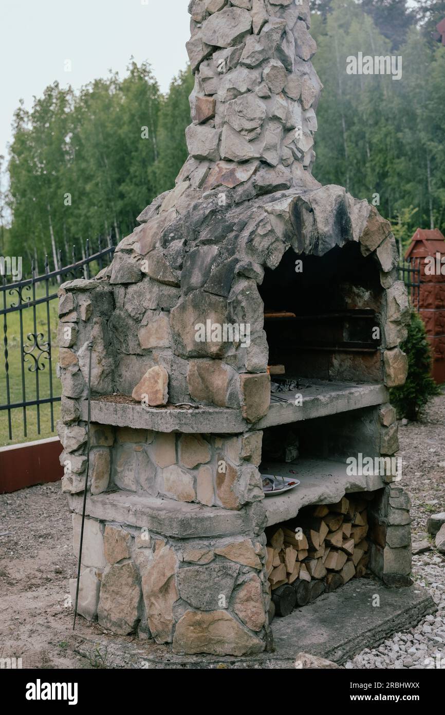 Steingrill im Garten mit Feuer - Zaun und Pflanzen im Hintergrund. Stockfoto