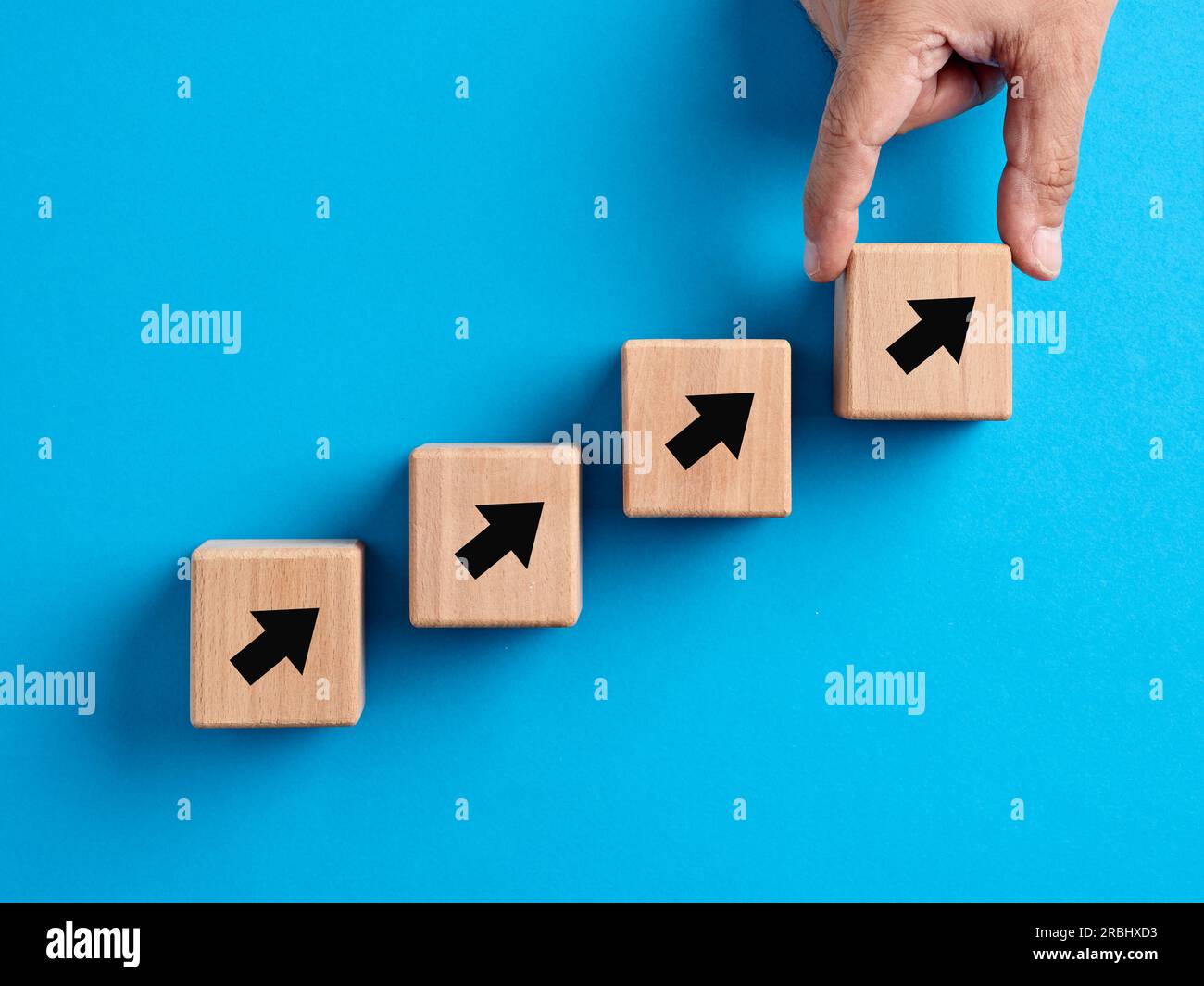 Business-, Finanz-, Leistungs- oder Karriereentwicklungs- und Verbesserungskonzept. Mit der Hand werden aufsteigende Pfeilsymbole in Stufen von Holzblöcken angeordnet. Stockfoto