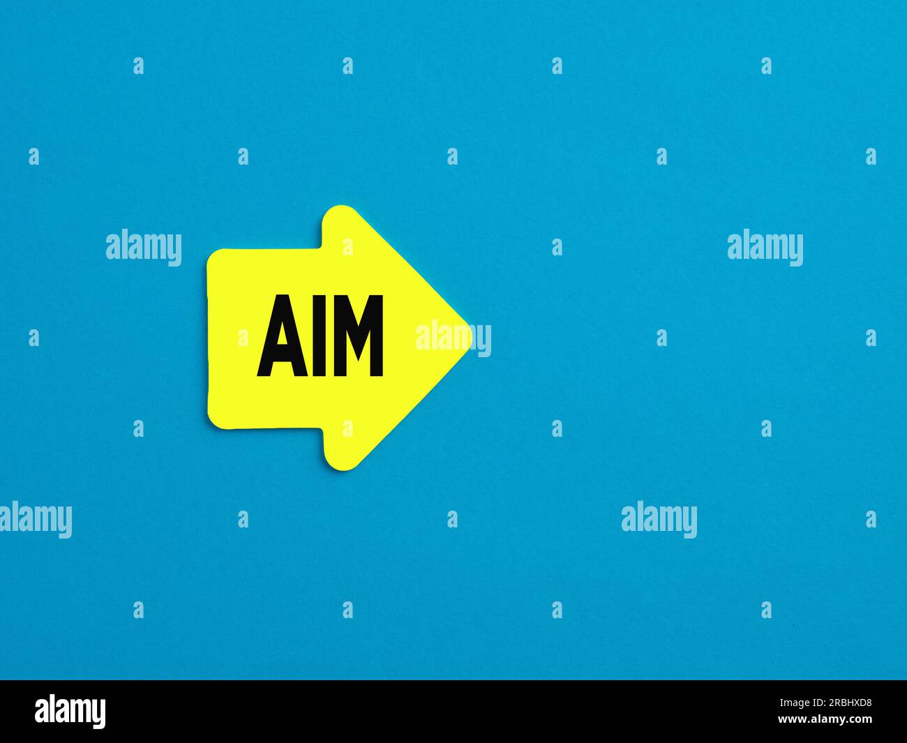Ziel, Ziel, Zweck, Entschlossenheit, Leistungskonzept. Gelber pfeilförmiger Aufkleber mit dem Wort „AIM“ auf blauem Hintergrund. Stockfoto