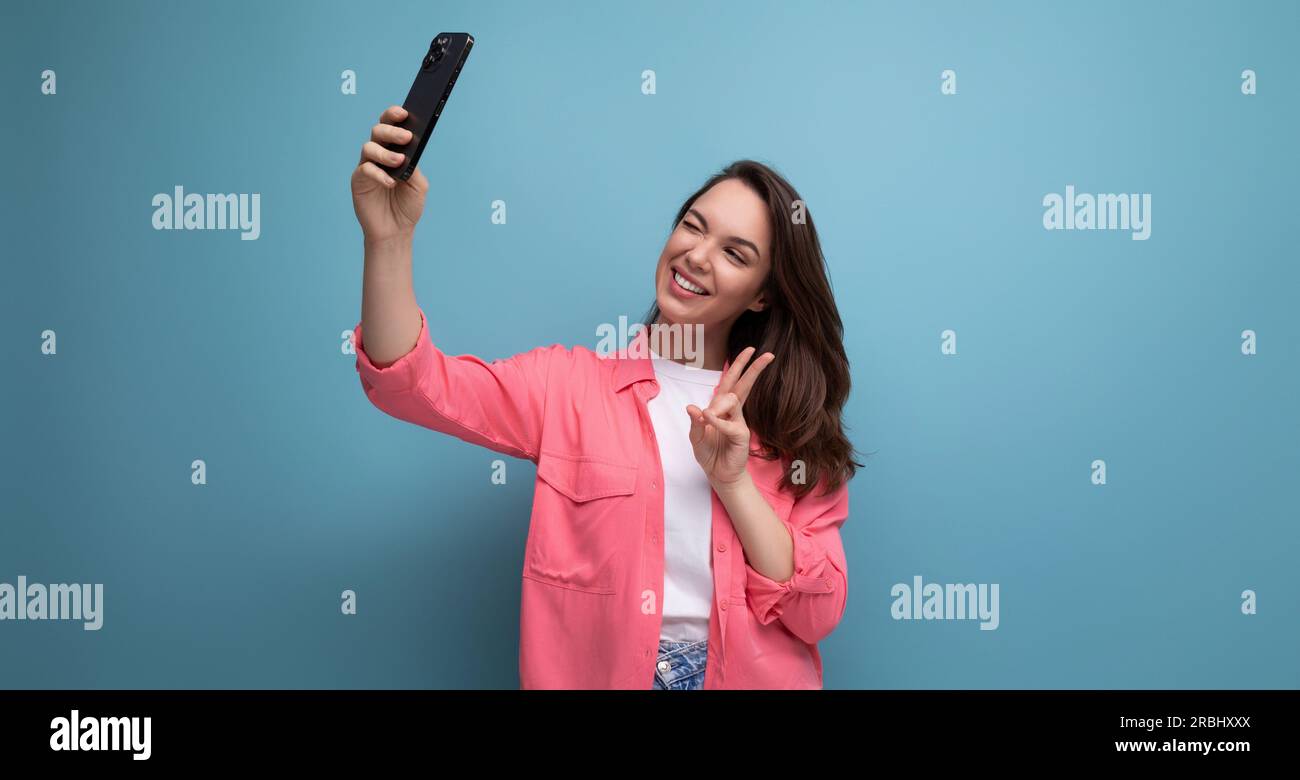 Eine moderne braune Frau mit pinkfarbenem Hemd macht Fotos mit dem Telefon im Studiohintergrund Stockfoto