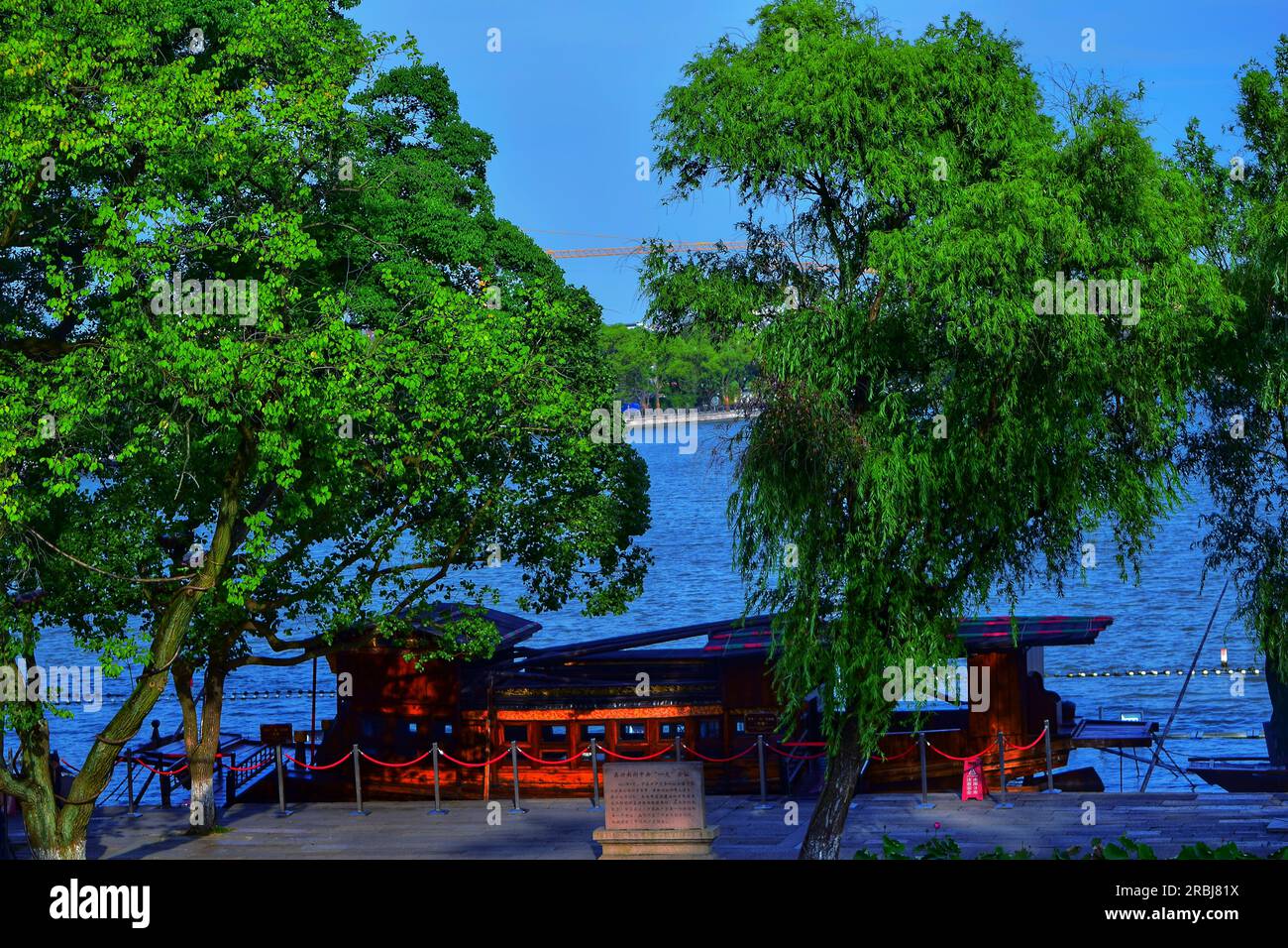 Erleben Sie die ruhige Schönheit, während ein traditionelles Boot anmutig entlang des Flusses segelt und sich in der warmen Umarmung des Sonnenlichts im Freien in China sonnt. Stockfoto