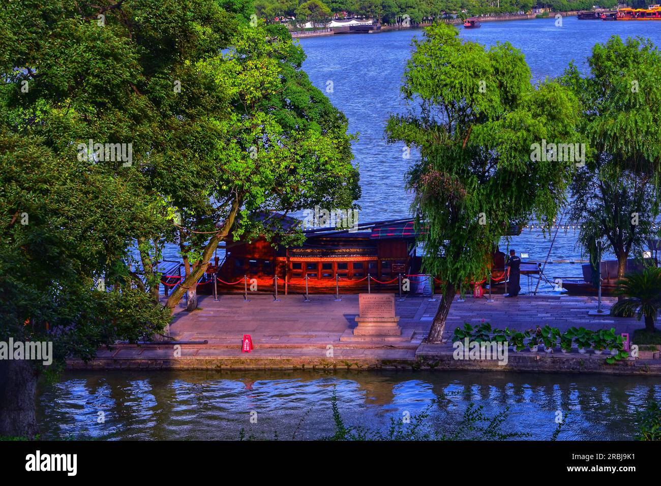 Erleben Sie die ruhige Schönheit, während ein traditionelles Boot anmutig entlang des Flusses segelt und sich in der warmen Umarmung des Sonnenlichts im Freien in China sonnt. Stockfoto