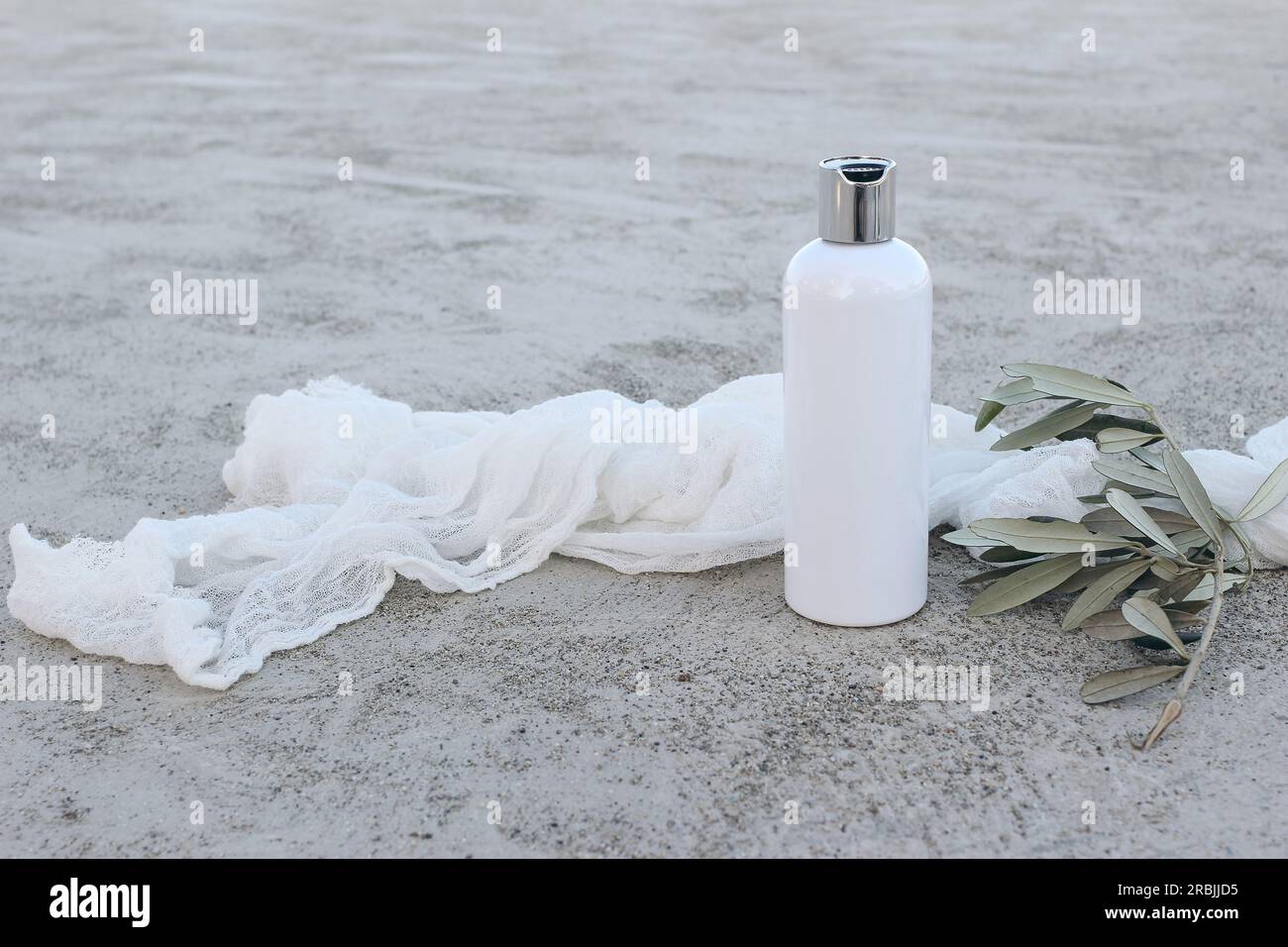Weißes kosmetisches Plastikfläschchen mit grünem Olivenbaumzweig und Moschlinschleier. Natürliche Flüssigseife, Shampoo oder Feuchtigkeitscreme. Grauer Grunge-Beton Stockfoto