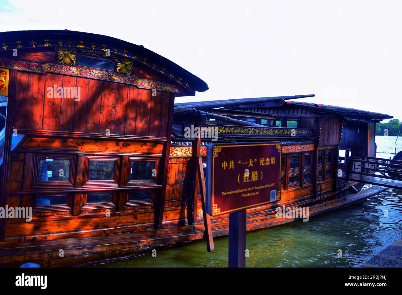 Erleben Sie die ruhige Schönheit, während ein traditionelles Boot anmutig entlang des Flusses segelt und sich in der warmen Umarmung des Sonnenlichts im Freien in China sonnt. Stockfoto
