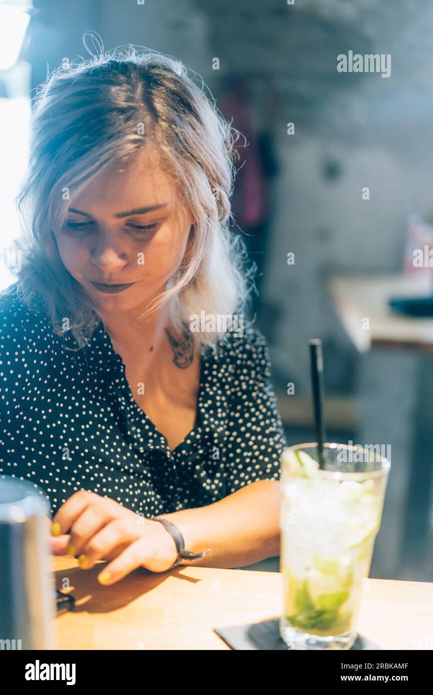 Blonde Girl überprüft ihr Telefon in Einer Cocktailbar. Stockfoto