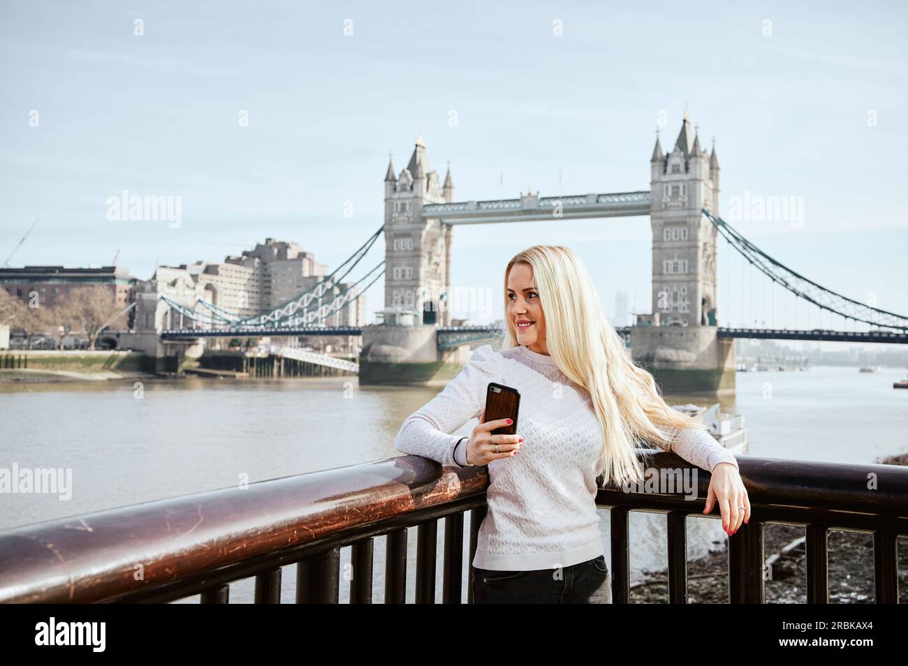 Eine attraktive Frau, die auf der Tower Bridge mit dem Handy herumschaut Stockfoto