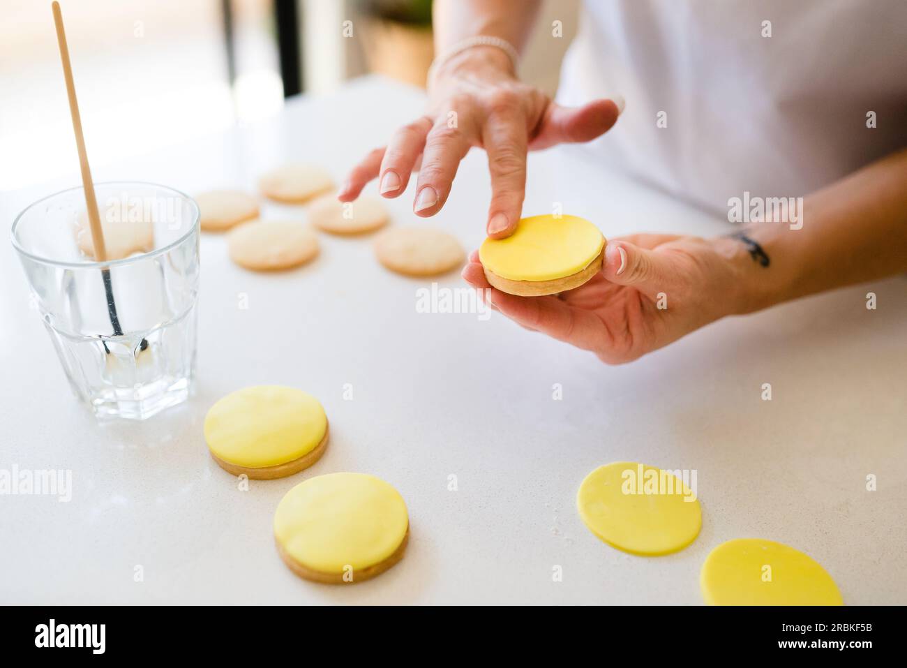 Die Hände einer Frau schmücken Kekse mit gelbem Fondant Stockfoto