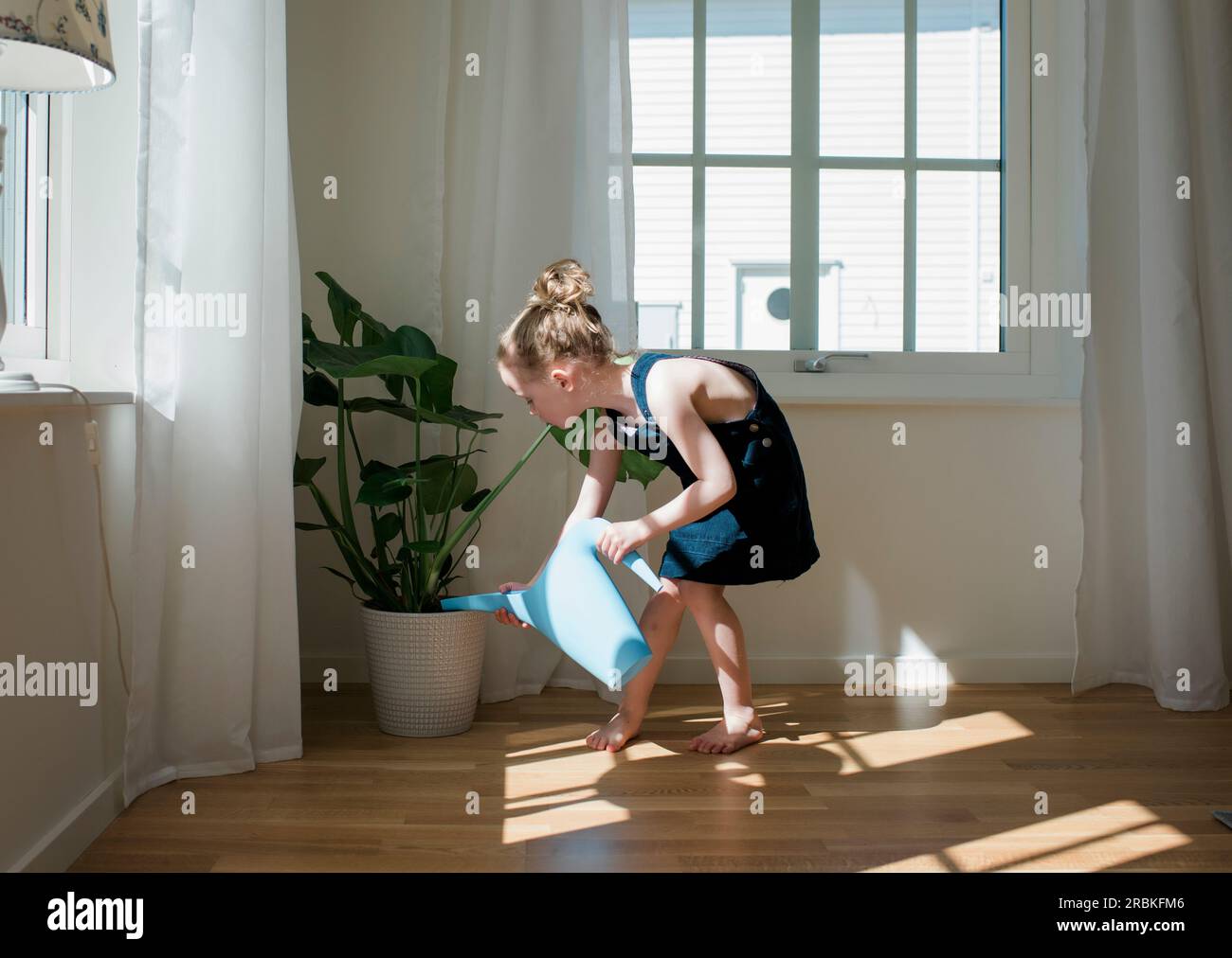 Ein junges Mädchen, das zu Hause die Pflanzen gießt Stockfoto